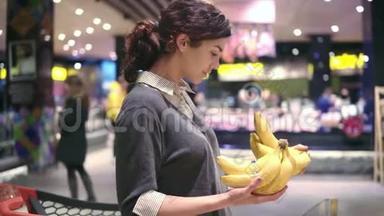 年轻漂亮的黑发女孩，20`正在摘香蕉，把香蕉放进<strong>水果店</strong>的购物车